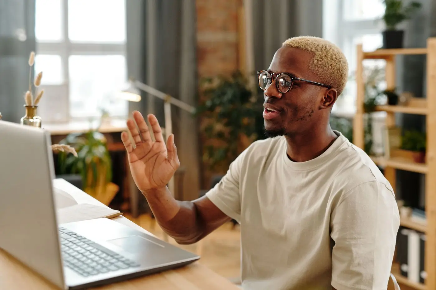 Man in glasses waving hello to his laptop at home