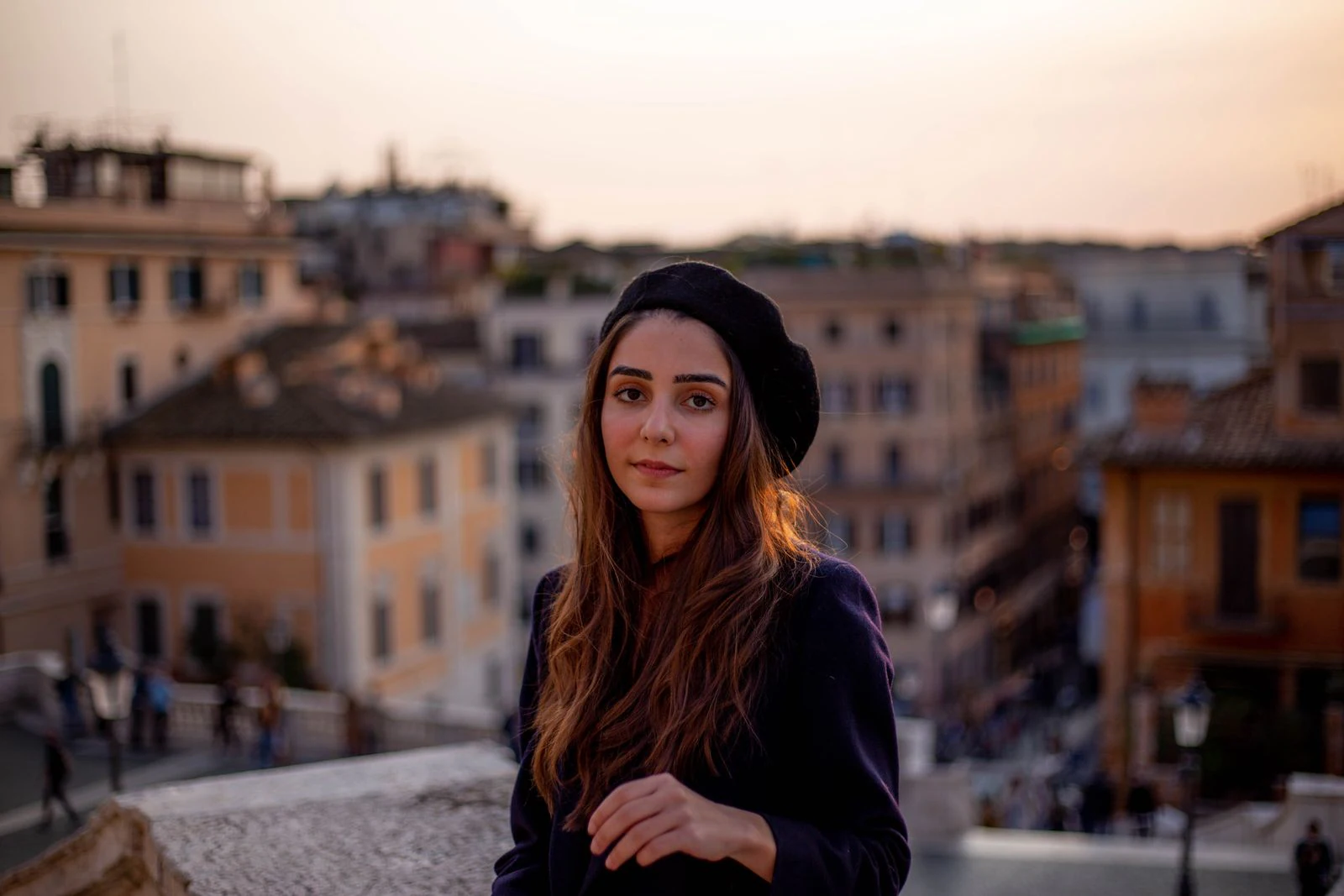 Giovane donna con un basco nero che guarda in camera, sullo sfondo i tetti di Roma al tramonto