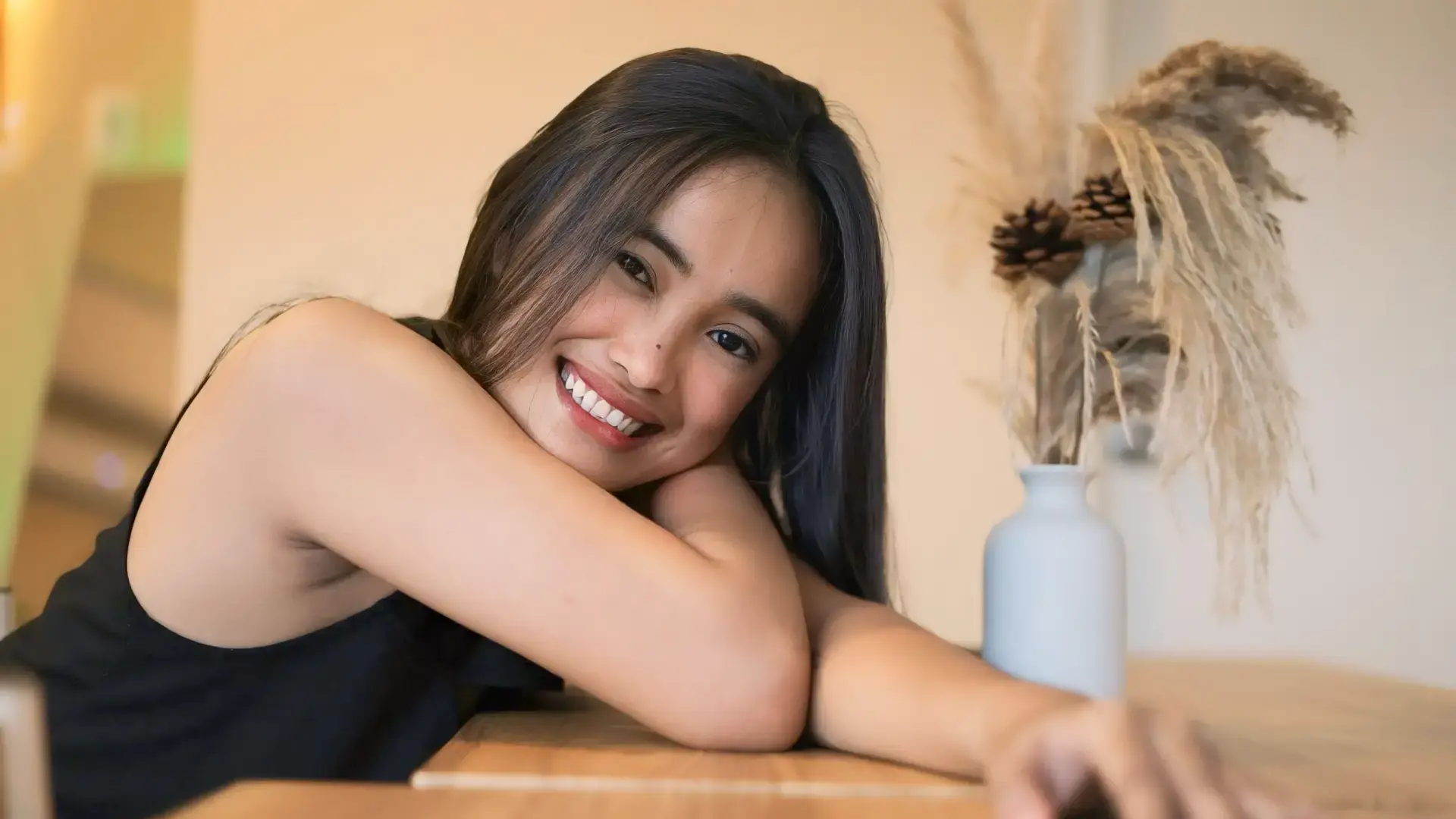 Smiling young woman resting her head on her arms at a table